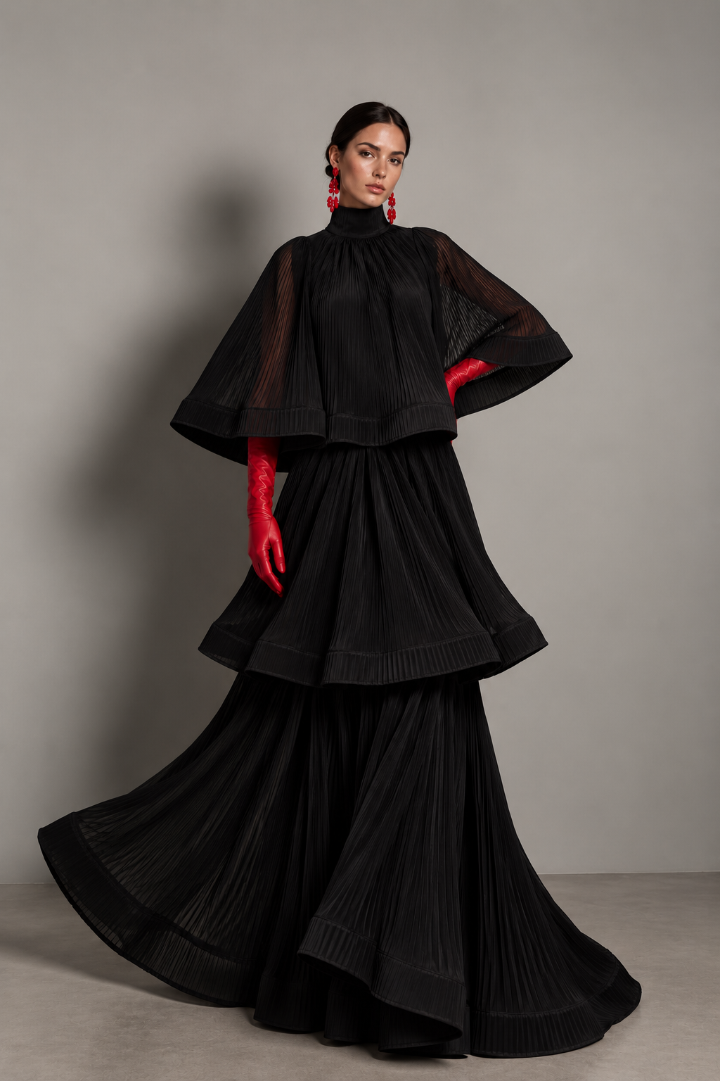 Black tiered, finely pleated cape-sleeve gown with a high mock-neck and a three-tier flared skirt.